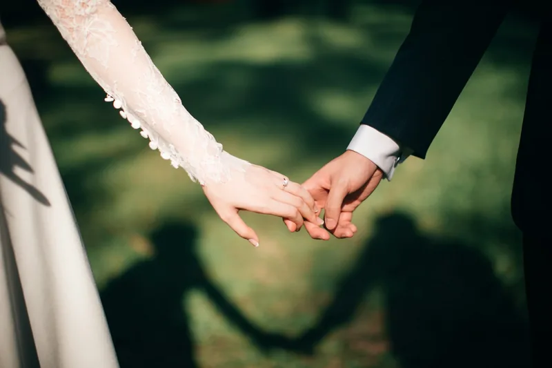 Manos de los novios y sus sombras en el pasto