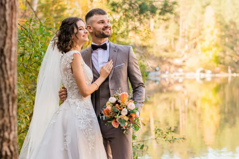 Novios frente a un lago con árboles de otoño