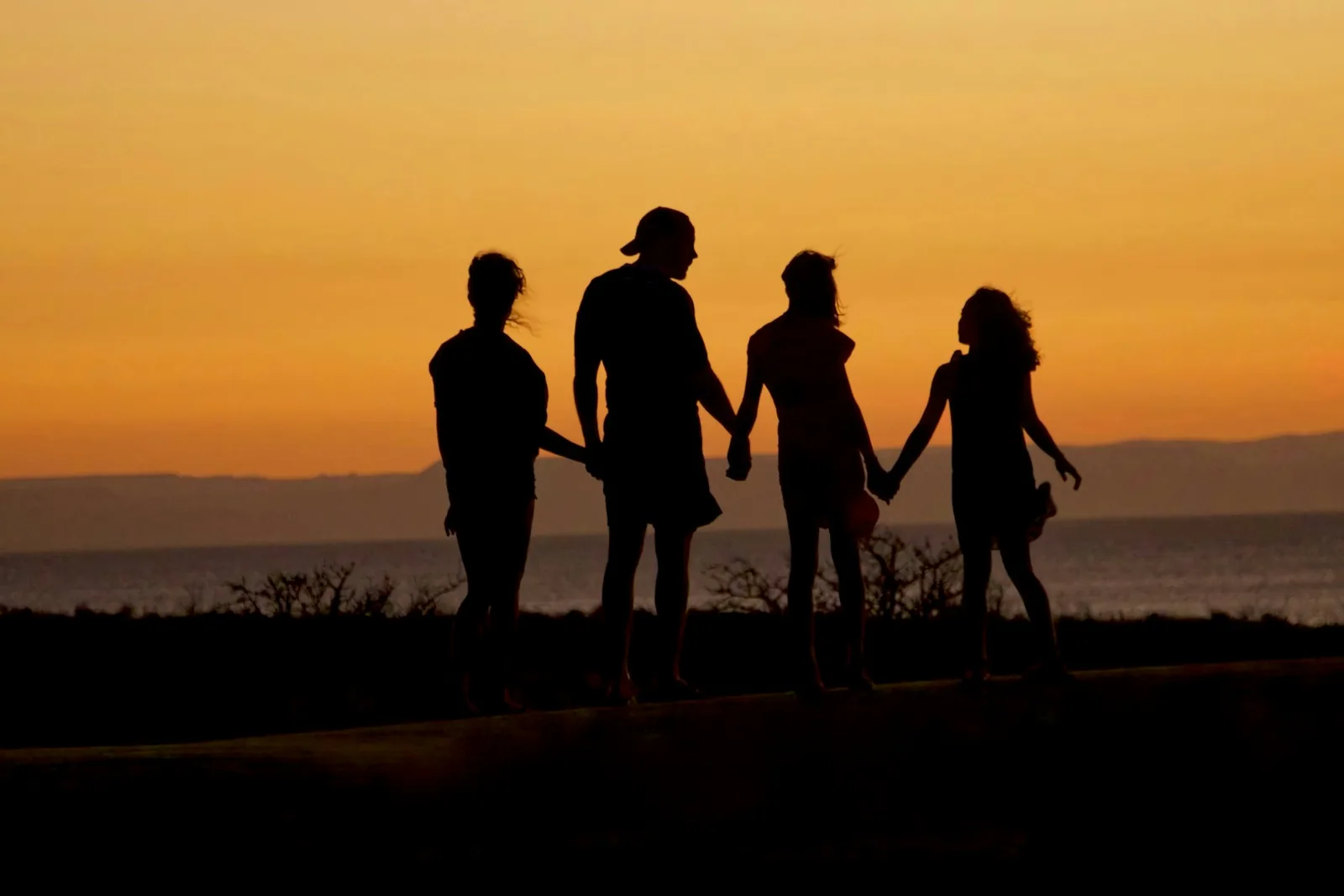 Familia de la mano frente al mar al atardecer